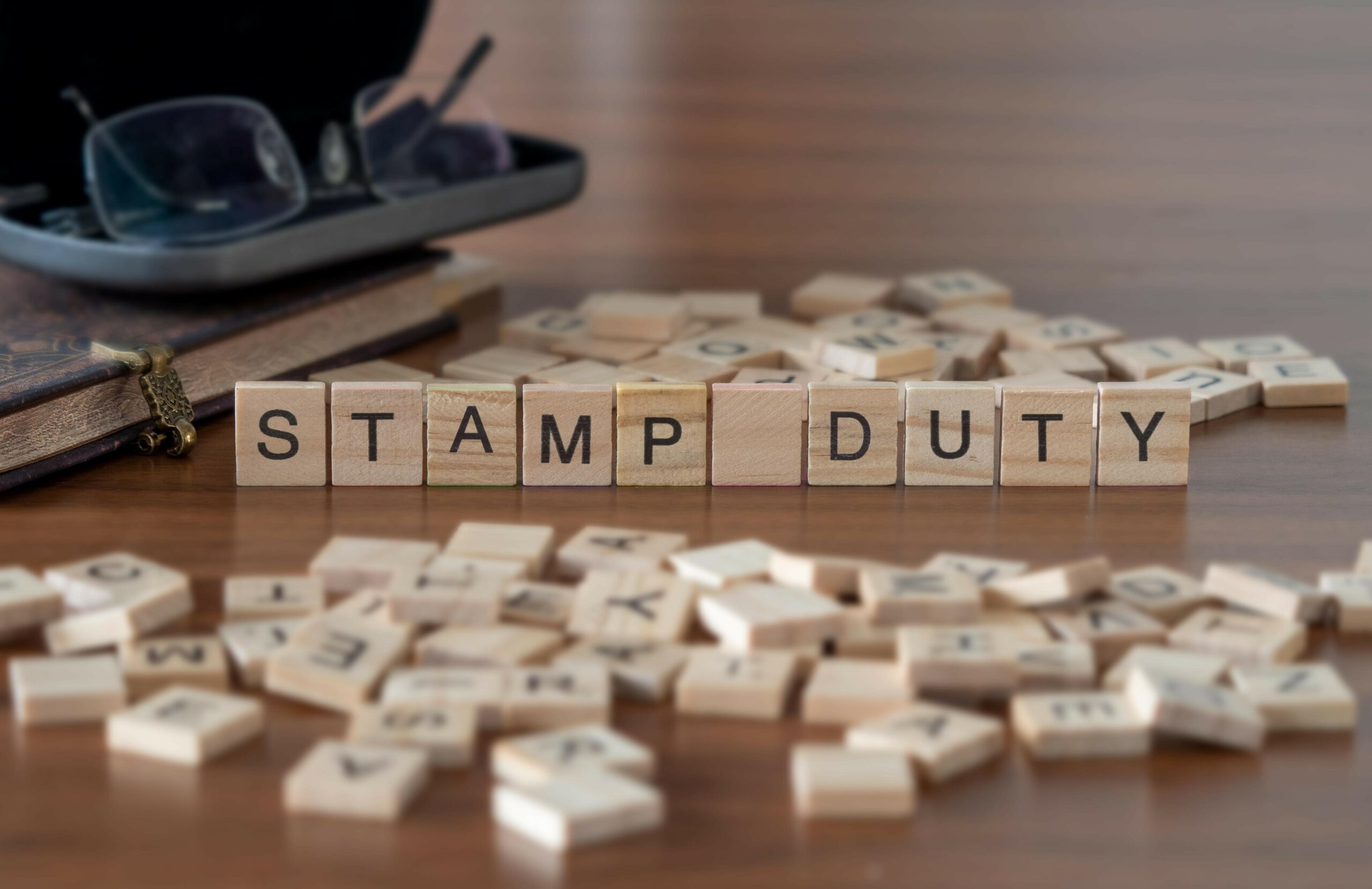 stamp duty word or concept represented by wooden letter tiles on a wooden table with glasses and a book